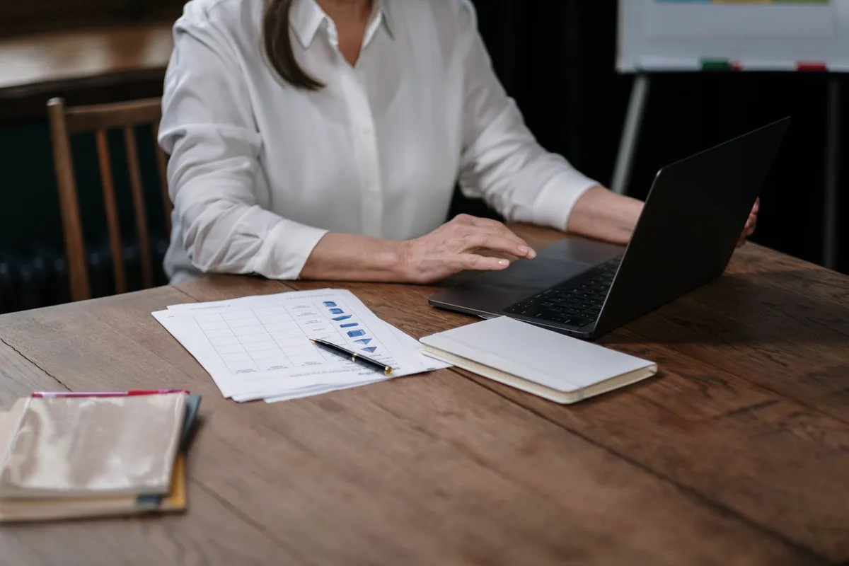 A woman at a home desk with a laptop and financial spreadsheets open, working remotely as a bookkeeping virtual assistant