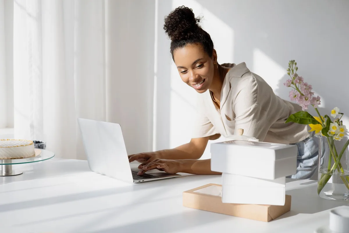 A woman typing on a laptop next to stacked product boxes ready to ship