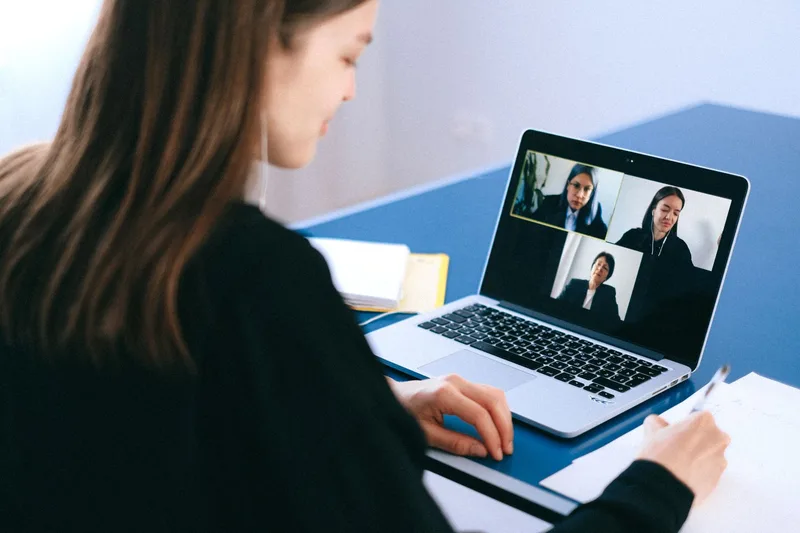 Woman conducting a remote video interview using a laptop at home, taking notes