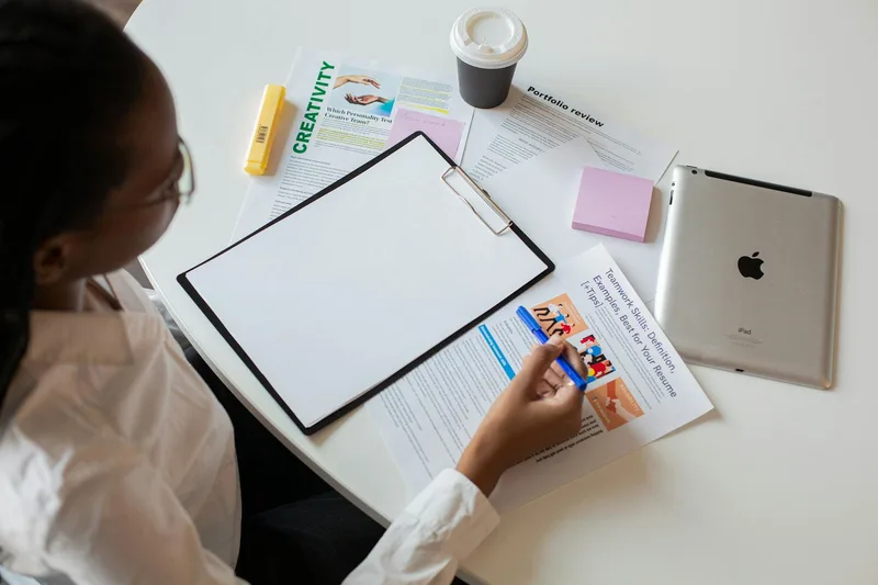 Person creating a digital portfolio on a laptop with a handwritten planning notebook beside them