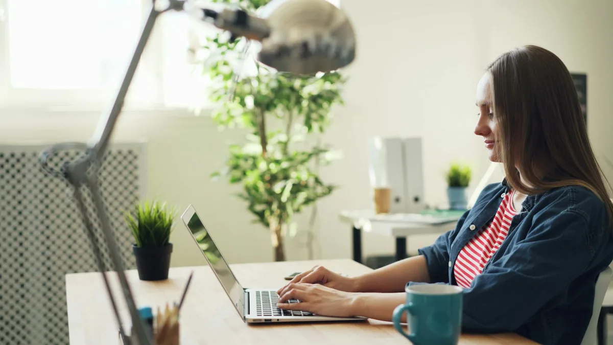 Woman working as a virtual assistant at a clean home desk with laptop and notebook