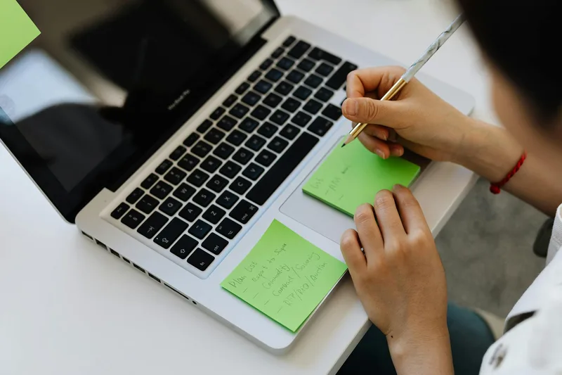 Person reviewing notes and organizing calendar tasks on a laptop at home
