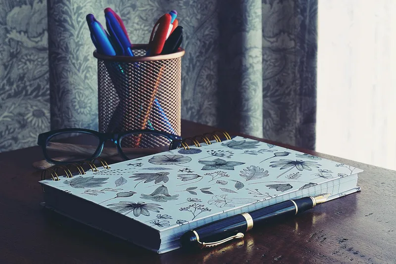Organized home office desk with a floral notebook, glasses, and pens — represents the planning and organization central to VA work