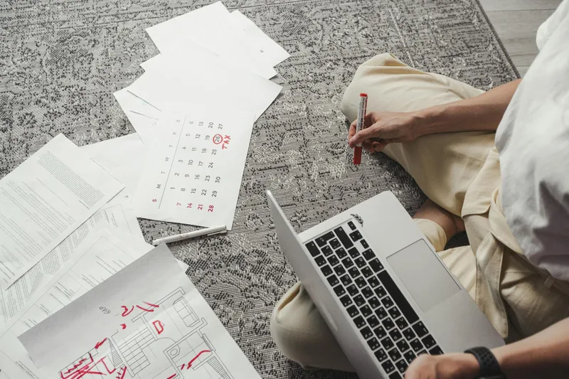 Man working on laptop surrounded by documents and a calendar, planning tasks for remote clients